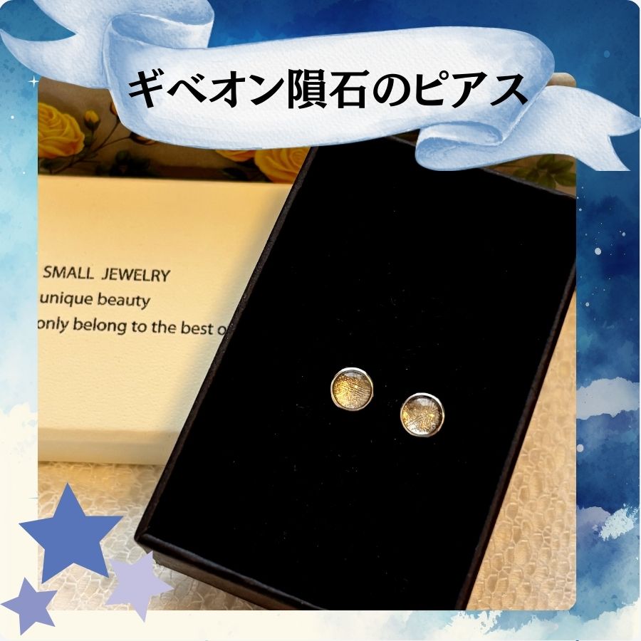 黒い台紙の上に置かれた、小さな丸いピアスの写真。ピアスの素材は隕石で、金色に近い輝きを持っている。画面上部には『ギベオン隕石のピアス』と日本語で書かれたリボン型の飾りが配置されている。背景は星空をイメージした青いデザイン。