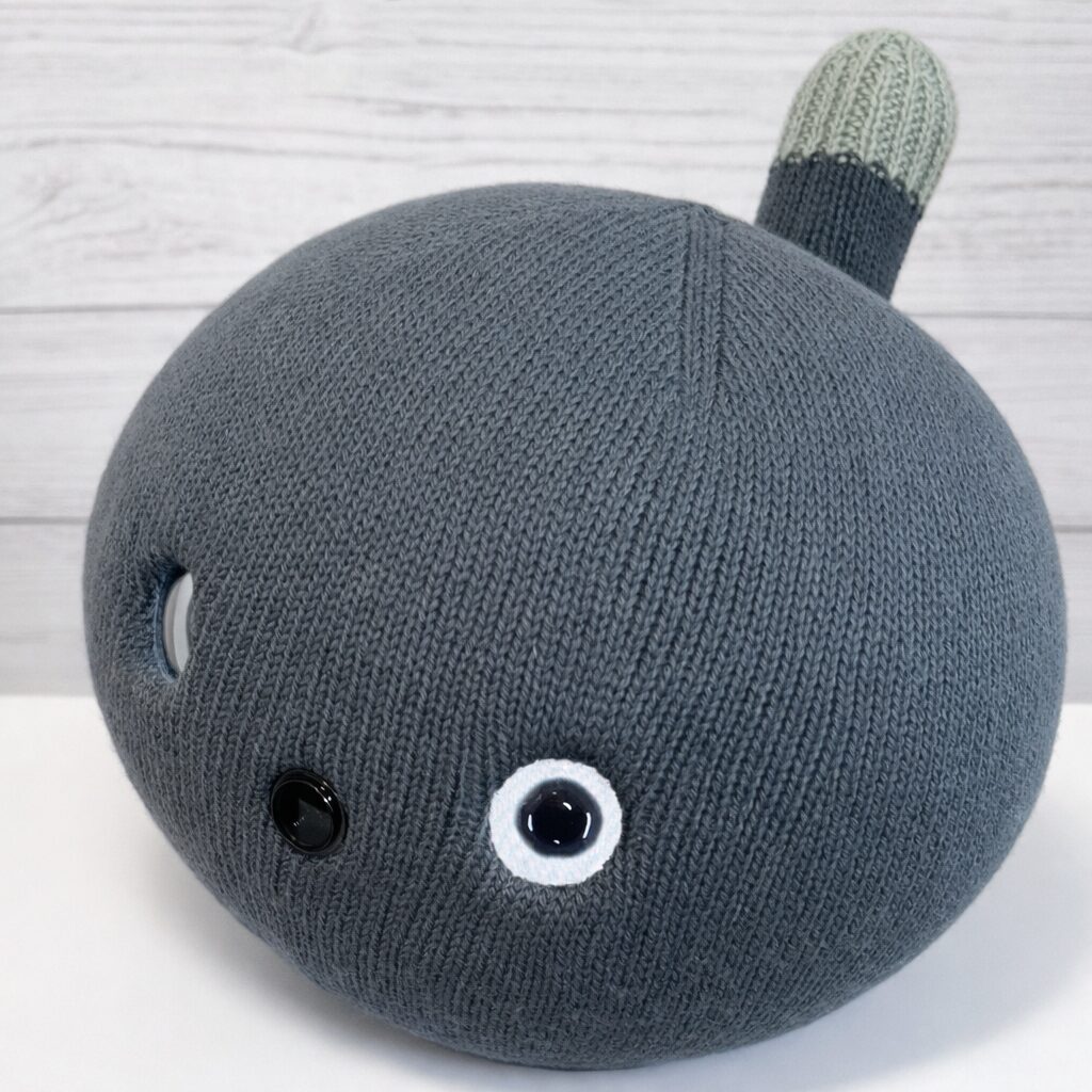 ニット素材の丸いボディを持つニコボが横を向いている写真。しっぽと目の配置が見える。
