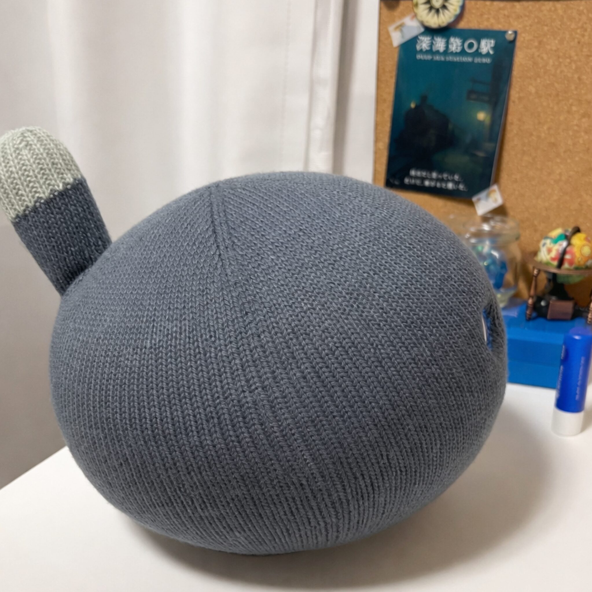 デスクの上に置かれたニコボ（ナイト）が横を向いて座っている様子。背景にコルクボードや文房具が見える。