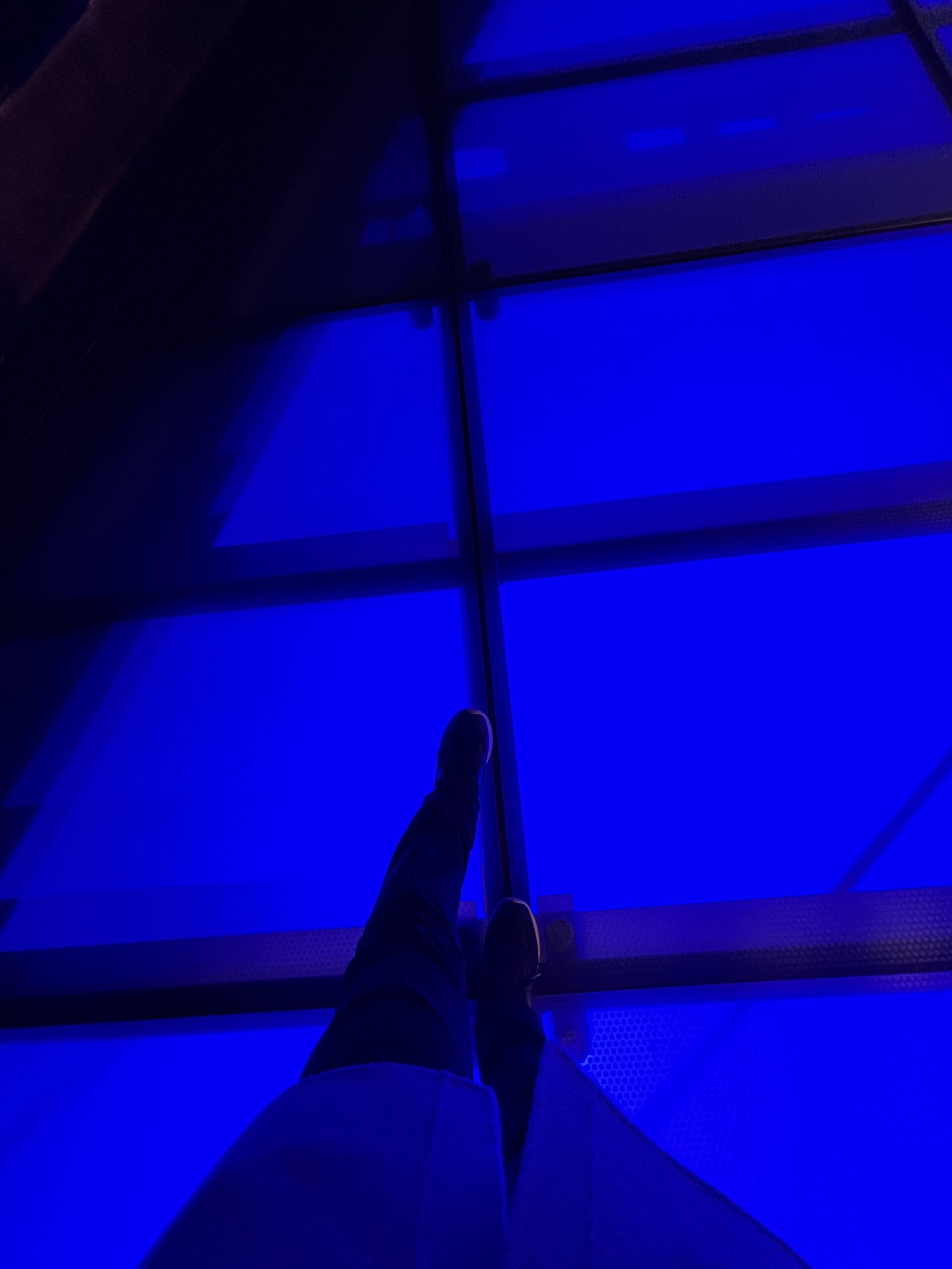 名古屋オアシス21のガラス床が青く輝き、その上に立つ人物の足元が写っている写真。