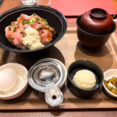 ローストビーフ丼の定食セット。ピンク色のローストビーフの上にソースが添えられ、卵、味噌汁、ポテトサラダ、漬物がトレイに並んでいる。