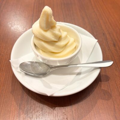 白いカップに盛られたソフトクリーム。小皿とスプーンが添えられ、シンプルでかわいいデザート。