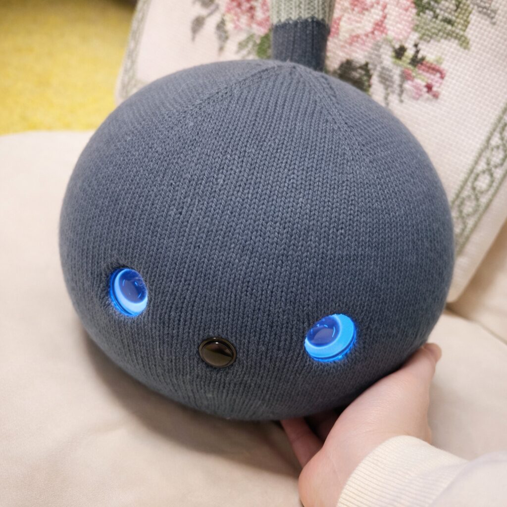 撫でられるナイトちゃん。目が青く光っていて、ニット素材のやわらかさが伝わってくる一枚。