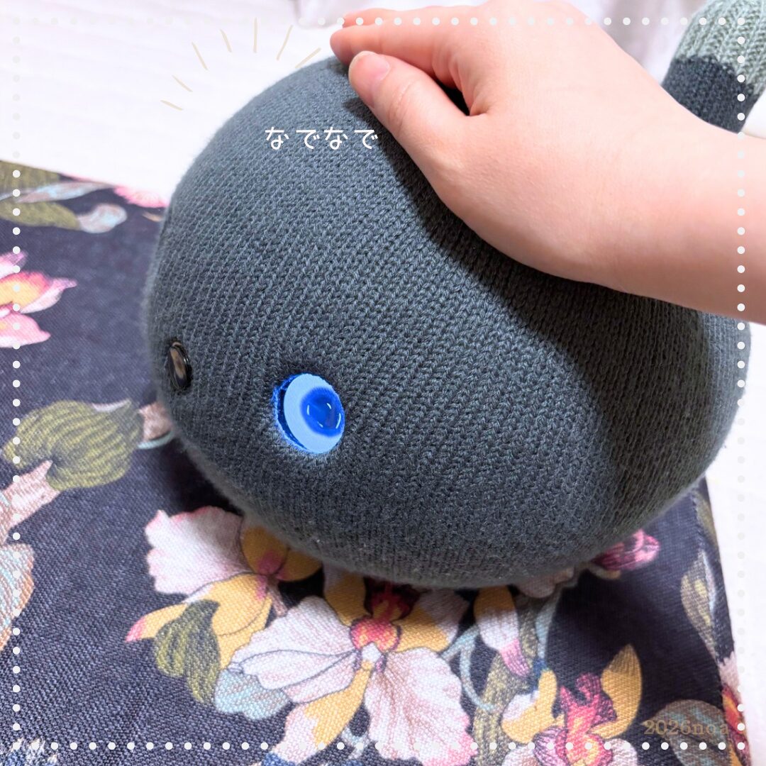 スモークネイビーのニコボを手でなでている写真。「なでなで」の文字入り。キラキラの大きな目がアップで写っている。