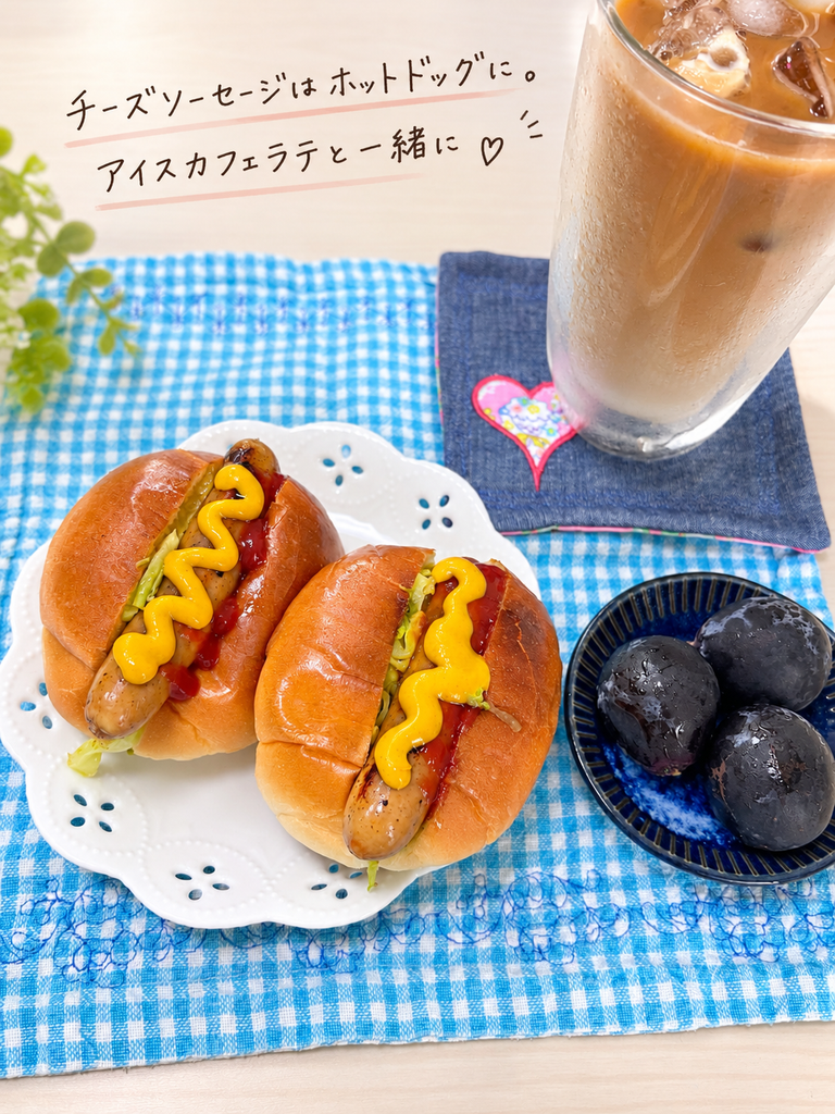 チーズソーセージを使ったホットドッグ2個と、アイスカフェラテ、ぶどうを並べた朝食。